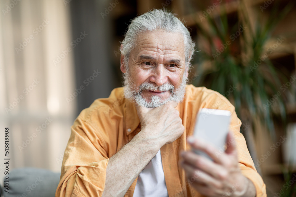 Cheerful senior man using smartphone at home Cheerful senior man using smartphone at home