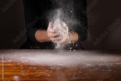 Mão espalmando farinha de trigo branca sobre mesa de madeira