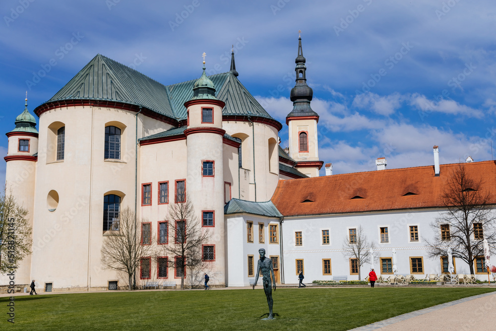 Litomysl, Czech Republic, 17 April 2022: Church of the Finding of the Holy Cross and Piarist dormitory near castle, baroque building with tower at sunny summer day, Fountain in Monastery Garden