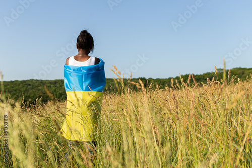 African american woman wrapped in ukrainian yellow blue flag flutters waving in the wind. National symbol of Ukraine. Stand with Ukraine, international support and solidarity