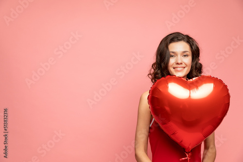 Portrait of young lady stands on pink background with heart shapped decoration © Yulia