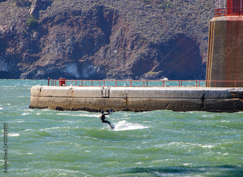 Brilliant kite surfing under the Golden Gate Bridge in Strong winds.  Surfer is shown against the concrete of the foundation. 