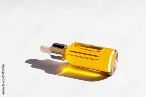Dropper glass Bottle Mock-Up with metal lid and yellow essential oil lying on white background. Eco-cream, serum, cosmetics, massage oil. Natural light, beautiful orange sun shadows. Copy Space