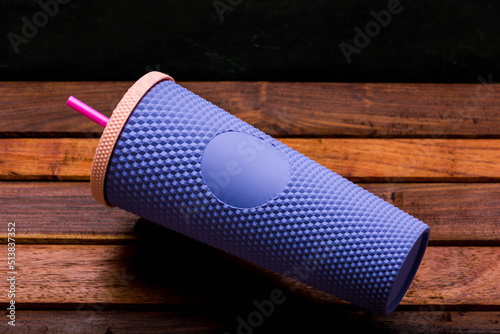 Large purple glass with a rough design, wooden lid and pink straw which is on a wooden table.