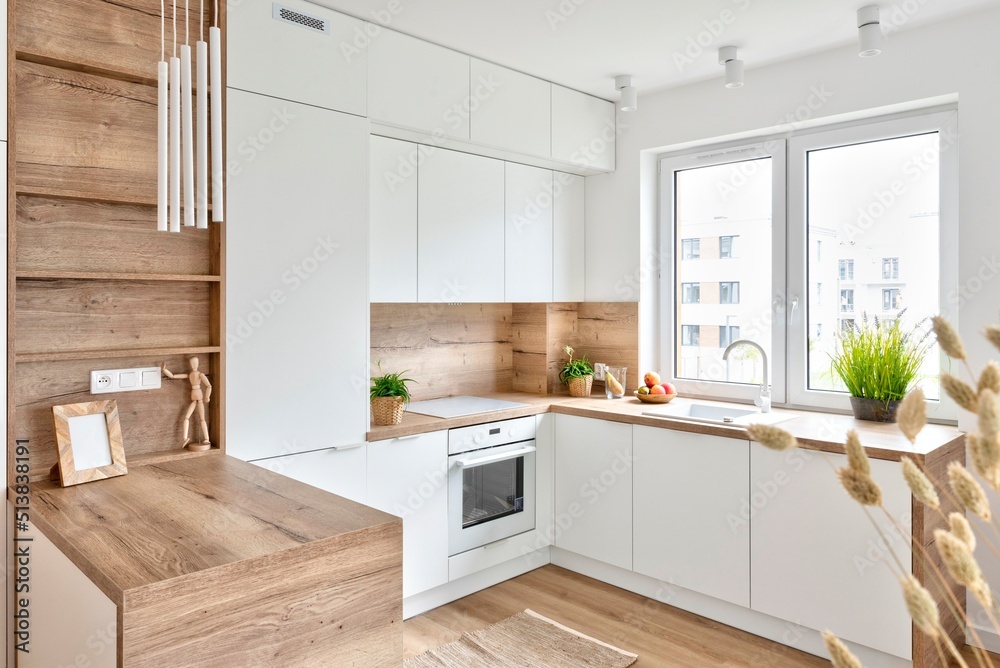 Modern interior of kitchen with white furniture, wooden counter and wooden floor. Kitchen sink with faucet near window and stylish design in new apartment. - obrazy, fototapety, plakaty 