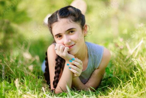 Obraz na płótnie Adorable little smiling girl lying on grass in garden and keeping her hand under chin w salonie