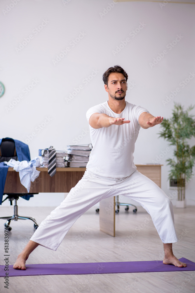 Fototapeta premium Young male employee doing sport exercises in the office