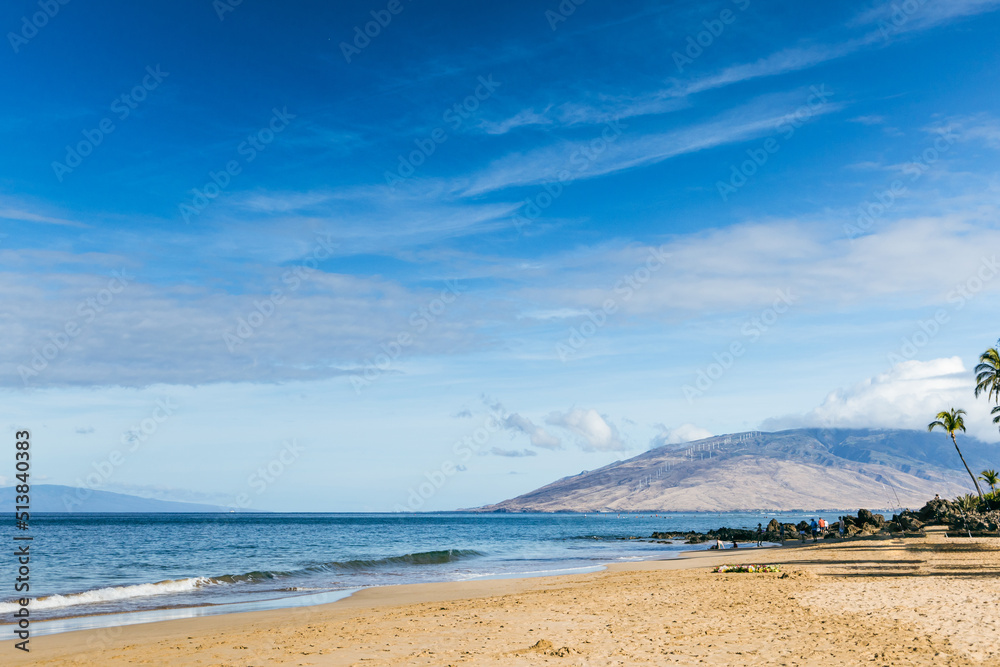 A beach in Maui Hawaii with sand, waves and a mountain in the distance