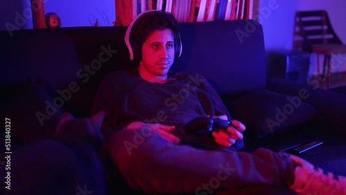 a man with a more serious tone in a medium shot plays video games in his apartme photo