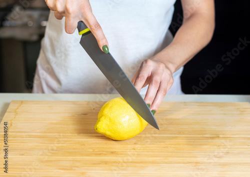 Close up of young woman hands cutting lemon on wooden cutting board at home. Young woman preparing healthy food.