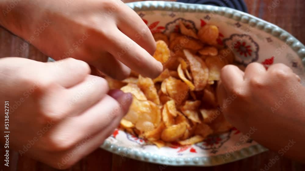 close-up overhead view grabbing bagged potato chips from a bowl with multiple hands at the same time close-up overhead view grabbing bagged potato chips from a bowl with multiple hands at the same time