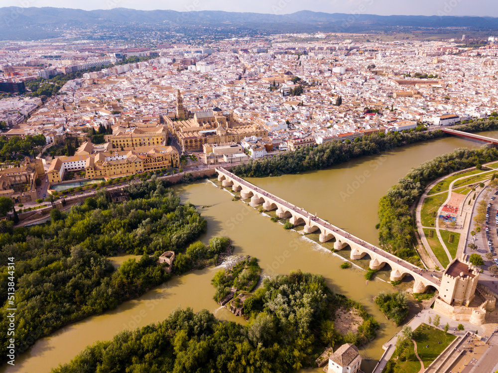 Scenic aerial view of ancient Roman bridge across Guadalquivir river and Moorish architecture of Mezquita-Catedral on background with Cordoba cityscape, Spain