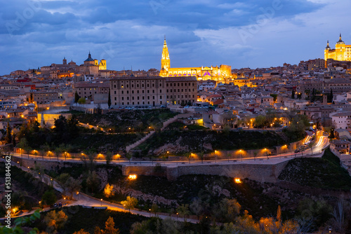 View of historic area of Toledo city on banks of Tagus River overlooking lighted Primatial Cathedral of Saint Mary and Alcazar fortress in spring twilight, Spain © JackF