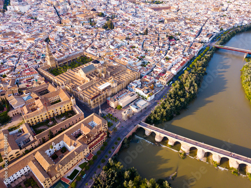 Aerial panoramic view of modern Cordoba cityscape on banks of Guadalquivir River with ancient pedestrian Roman Bridge and Mosque-Cathedral, Spain..