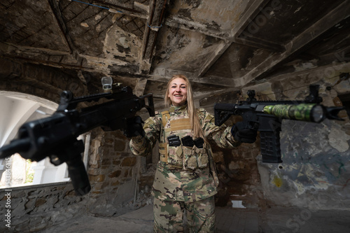 Caucasian woman in army uniform holding two machine guns. 