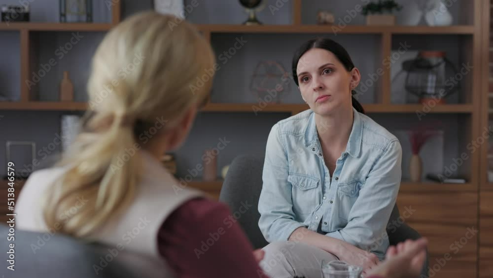 Over shoulder view of female psychologist sitting in armchair, talking with upset woman patient. Psychologist taking notes on clipboard. Psychology, mental therapy, mental health, therapy session. Over shoulder view of female psychologist sitting in armchair, talking with upset woman patient. Psychologist taking notes on clipboard. Psychology, mental therapy, mental health, therapy session.