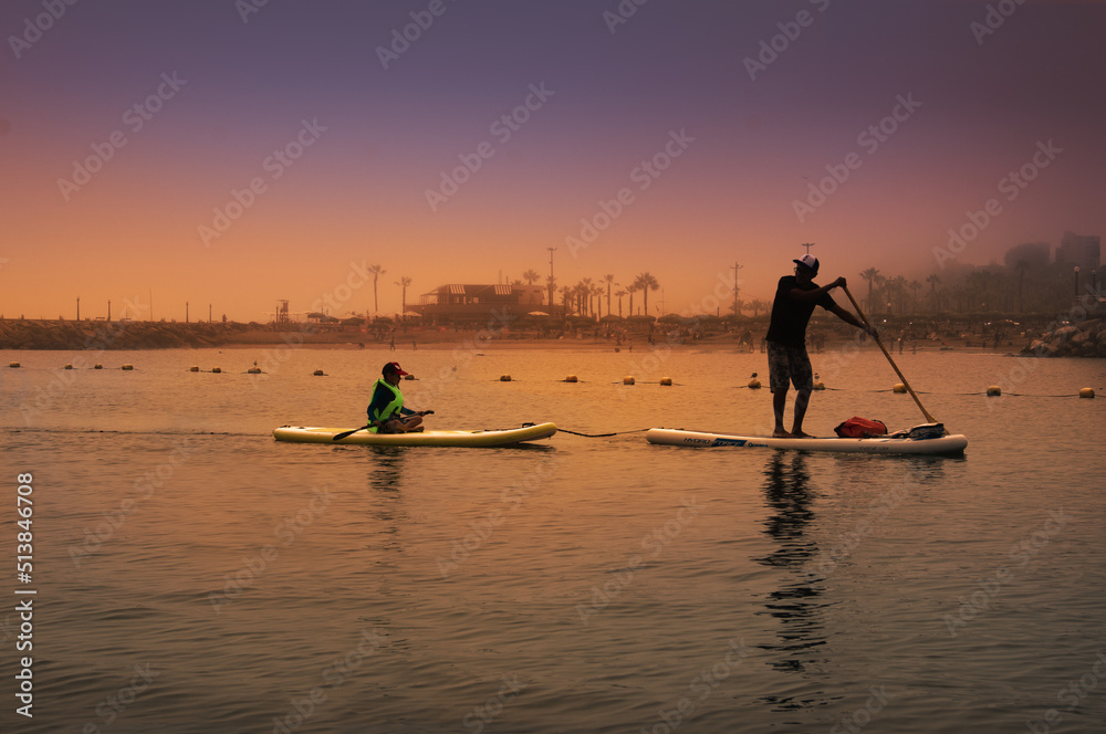 Naklejka premium father and son surfer rides by paddle board (S.U.P.) in the ocean against the background of costa verde (lima,peru) on sunset
