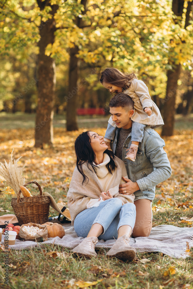 Fototapeta premium Portrait of happy young family sitting on plaid together in autumn park