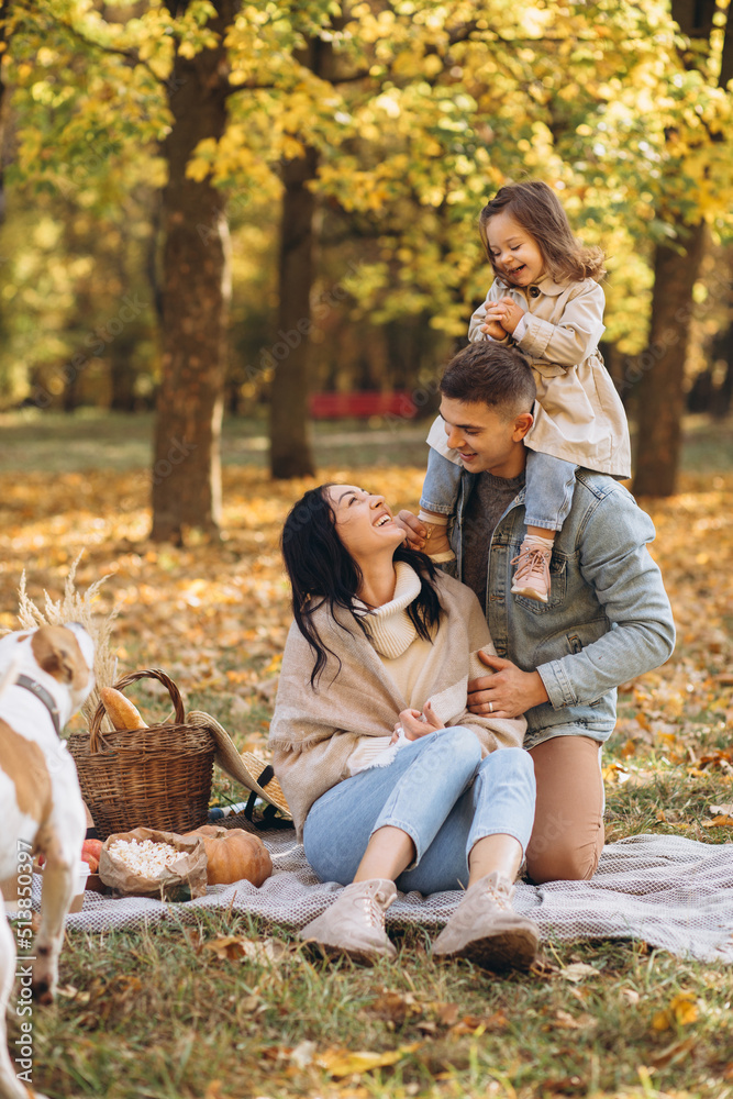 Fototapeta premium Portrait of happy young family sitting on plaid together in autumn park