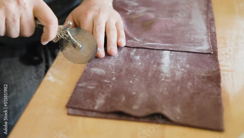 Man slices beet purple pasta dough into even sheets using a roller blade