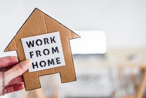 work from home sign being hold in front of out of focus home office desk setup, digital nomads working remotely or wfh days during lockdowns