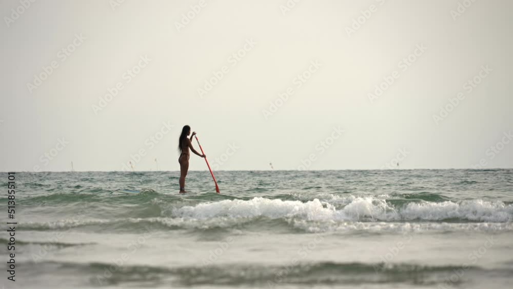 Woman Standing On Paddleboard And Rowing Out To Sea Woman Standing On Paddleboard And Rowing Out To Sea