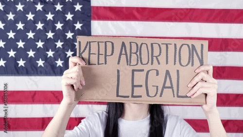 Young woman protester holds cardboard with Keep Abortion Legal sign against USA flag on background. Girl protesting against anti-abortion laws. Feminist power. Equal opportunity Womens rights reedom. photo