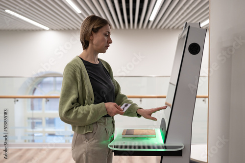 Middle-aged woman using self-service terminal in digital library space, registering book, searching and selecting literature or browsing catalogue. Innovative technologies in libraries photo