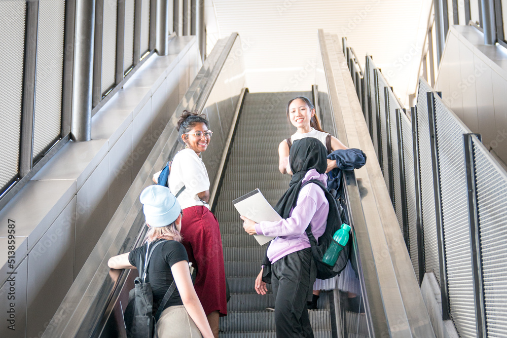 Group of happy young female students going up the escalator.