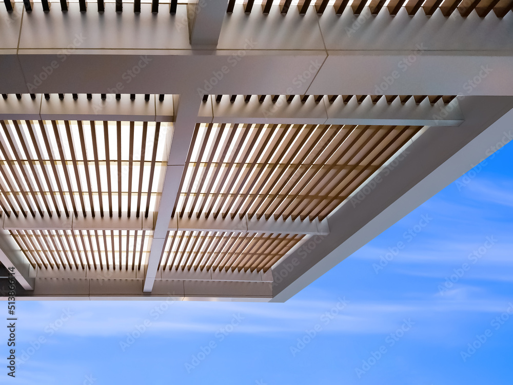 Low angle view of modern battens roof awning outside of building against blue sky background Low angle view of modern battens roof awning outside of building against blue sky background