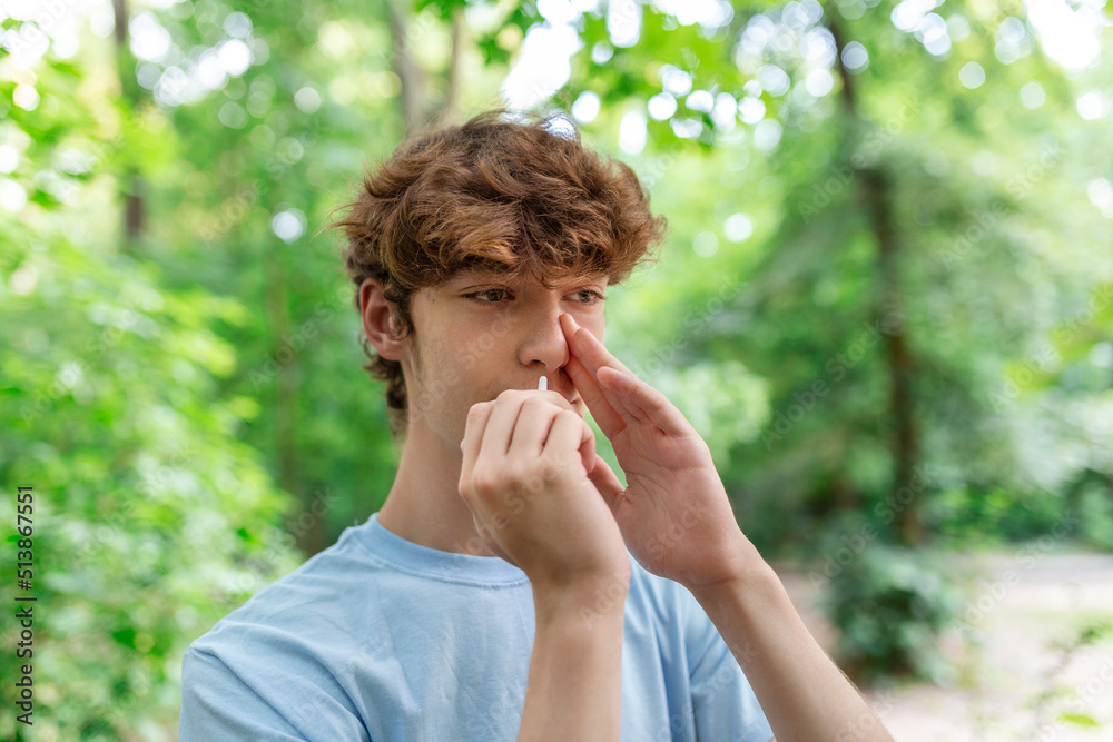 Young man is Using Nasal Spray Due to the Problems with Nose and Breathing in the Public Park. Young man is Using Nasal Spray Due to the Problems with Nose and Breathing in the Public Park.