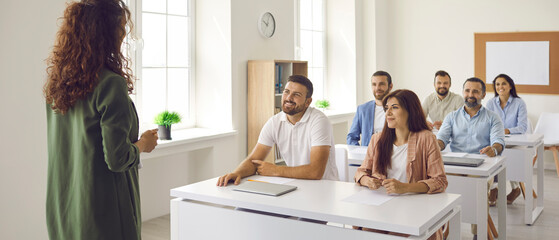 Experienced female teacher who specializes in adult education teaches a lesson to adult students. Woman teaches a variety of women and men by sharing knowledge, experience and information with them.