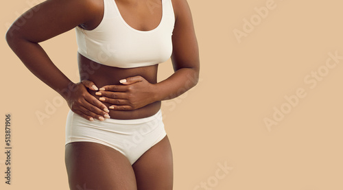 Crop of African American woman on yellow studio background suffer from appendicitis spasm. Pain in right lower stomach part. Unhealthy black female have acute ache in belly need hospitalization. photo