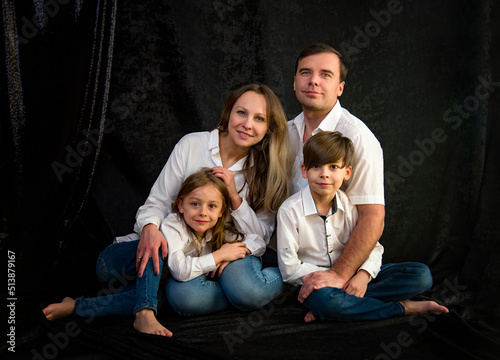 portrait of happy family with two kids in white shirts and blue jeans in studio on black background