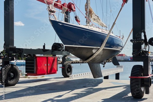 Billede på lærred Blue sloop rigged sailboat lifted by a crane being placed back in the water after winterization