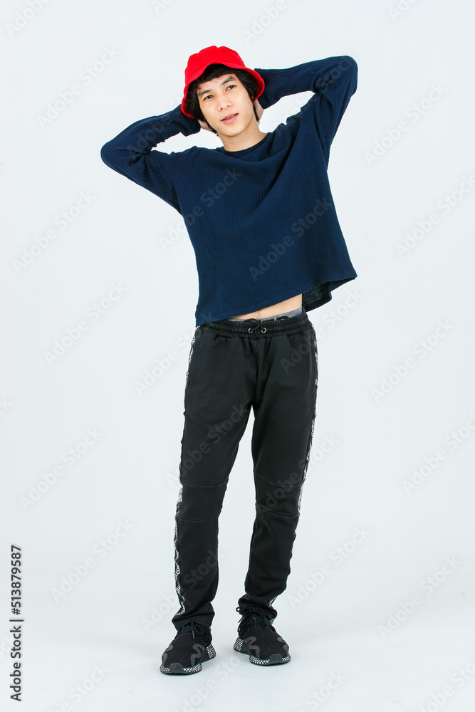 Full body studio shot Asian young handsome slim teenager fashion male model in street style outfit long sleeve shirt standing posing smiling holding hand adjusting red bucket hat on white background Full body studio shot Asian young handsome slim teenager fashion male model in street style outfit long sleeve shirt standing posing smiling holding hand adjusting red bucket hat on white background