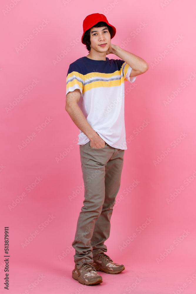 Portrait studio shot of Asian young handsome urban teenager fashion male model in street style outfit t shirt sport beige pants and red bucket hat standing posing look at camera on pink background Portrait studio shot of Asian young handsome urban teenager fashion male model in street style outfit t shirt sport beige pants and red bucket hat standing posing look at camera on pink background