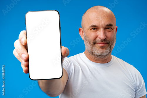 Middle-aged man showing blank smartphone screen with copy space against blue background photo