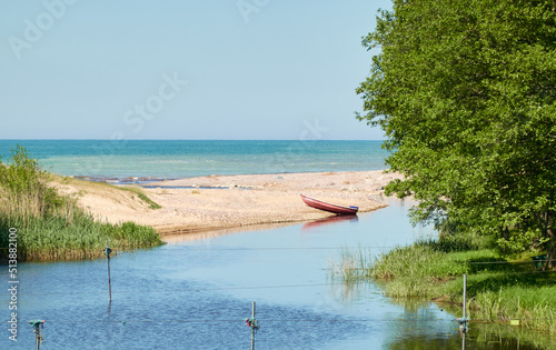 Small boat standing on the beach (sand dunes). River flowing into the Baltic sea. Clear blue sky, reflections on water. Nature, ecology, ecotourism, sport, wanderlust, boating, fishing, swimming theme photo