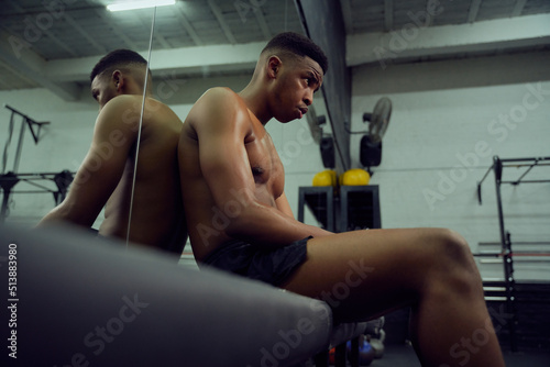 Young African American male athlete resting in the gym after a hard cross training. Shirtless mixed race male sitting down after exercising. High quality photo