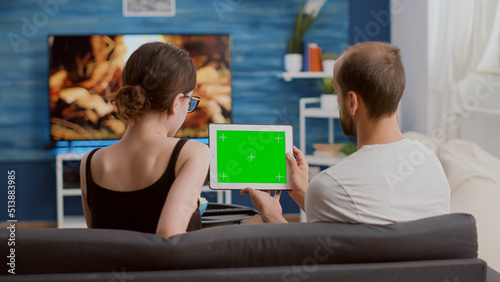 Man holding digital tablet with green screen watching online video content with girlfriend sitting on sofa. Couple looking at touchscreen device with chroma key enjoying influencer vlog.