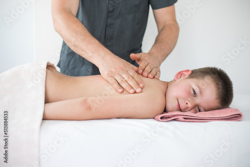 Boy toddler relaxes from a therapeutic massage. Physiotherapist working with patient in clinic to treat the back of a child