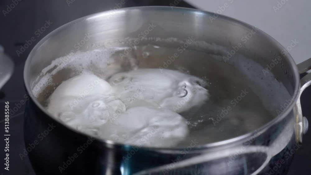 Chicken white eggs are boiled in boiling water in a metal saucepan. Close up Chicken white eggs are boiled in boiling water in a metal saucepan. Close up