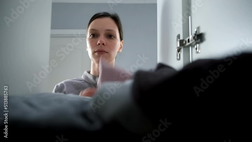 Young woman takes clothes from the closet, closeup view. She is opening and closes the wardrobe door, shooting from inside the closet. Everyday life and routine in city apartment.