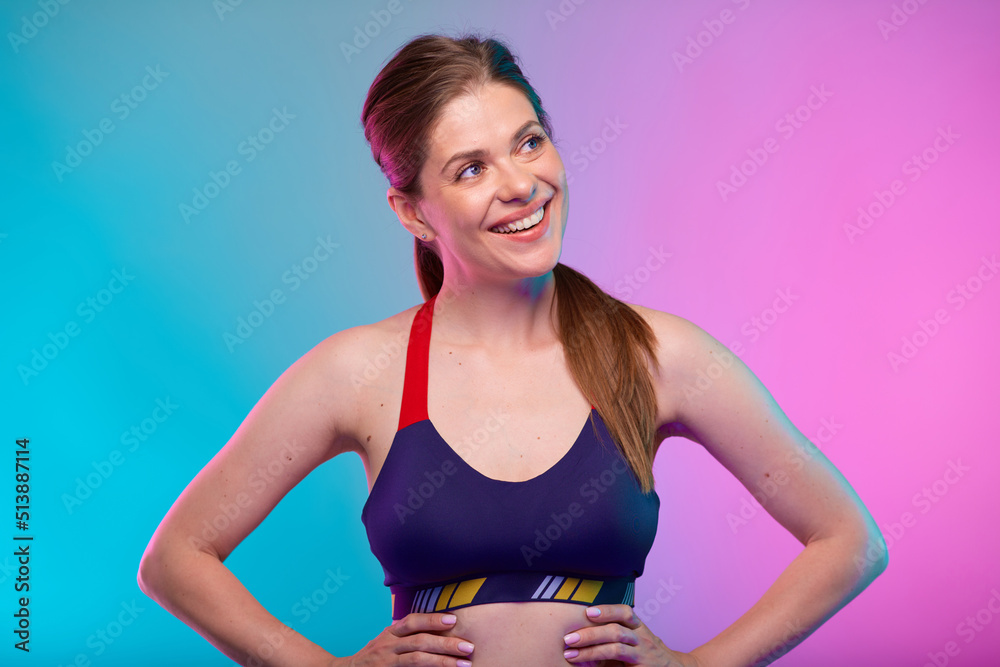 Smiling sporty woman in fitness bra sportswear with hands on waist looking up. Female fitness portrait isolated on neon multicolor background. Smiling sporty woman in fitness bra sportswear with hands on waist looking up. Female fitness portrait isolated on neon multicolor background.