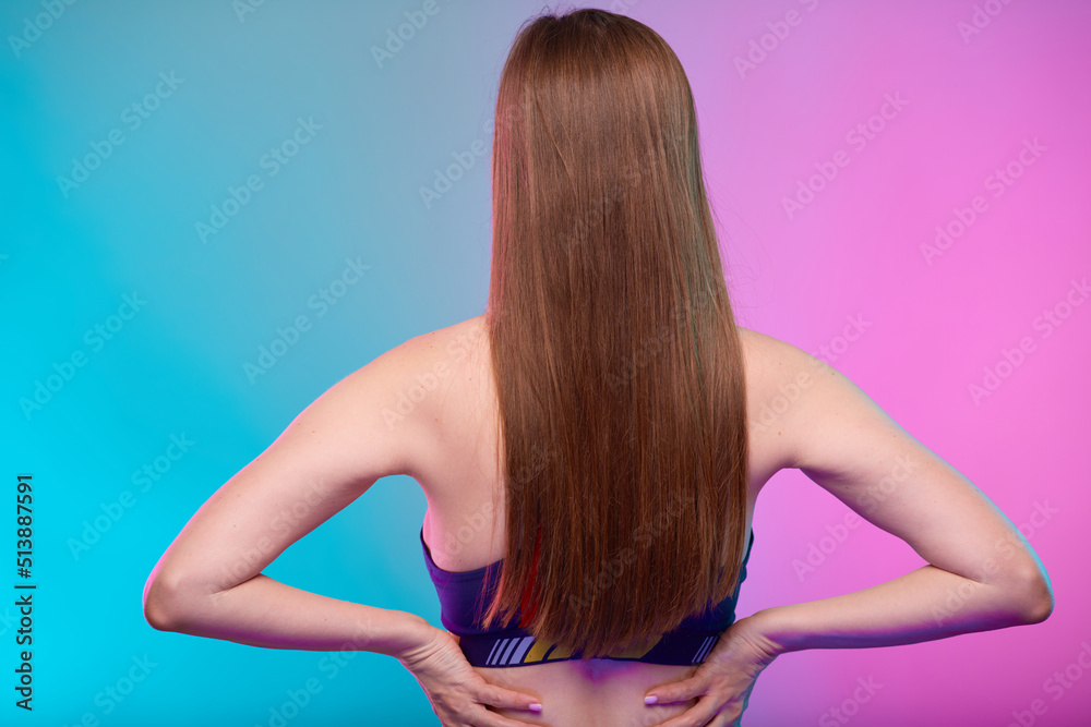 Sporty woman with long hair in fitness sportswear back view with arms on waist. Female fitness portrait isolated on neon multicolor background. Sporty woman with long hair in fitness sportswear back view with arms on waist. Female fitness portrait isolated on neon multicolor background.