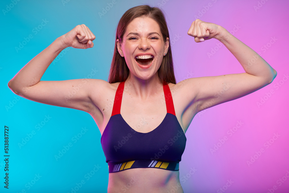 Happy emotional sporty woman in fitness sportswear flexes arms and demonstrates muscles. Female fitness portrait isolated on neon multicolor background.
