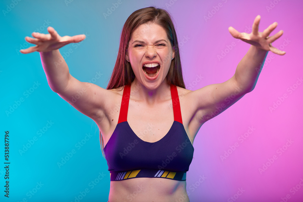 Power muscle concept with sporty shouting woman in fitness sportswear flexes her arm. Female fitness portrait isolated on neon multicolor background.