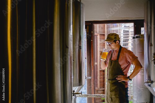 Young male brewer holding a glass of beer in hand Eating craft beer to check the taste and color of the beer in the craft brewery.