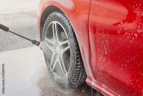 Washing red car in a self-service car wash station. Wheel and tire rubber closeup. Car wash self-service.